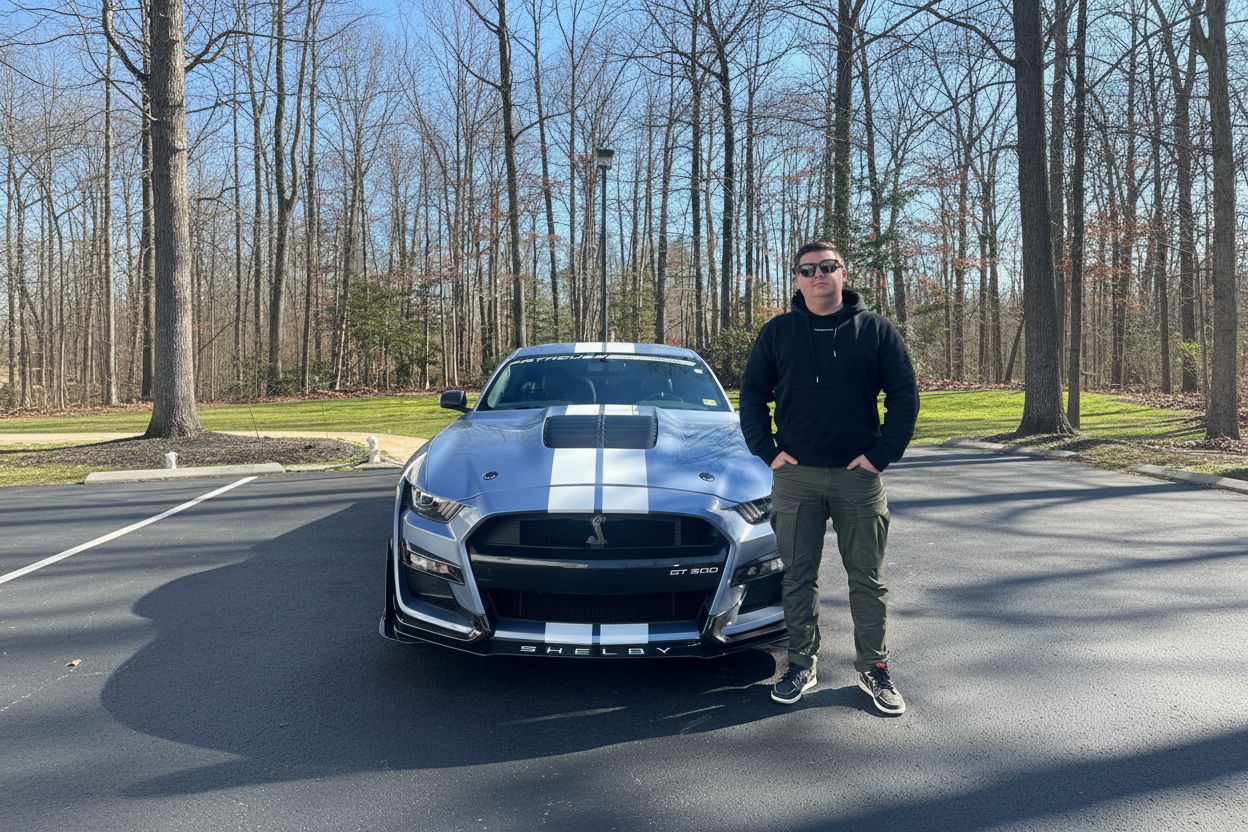 Person standing next to a Shelby GT 500 car on a road with trees in the background