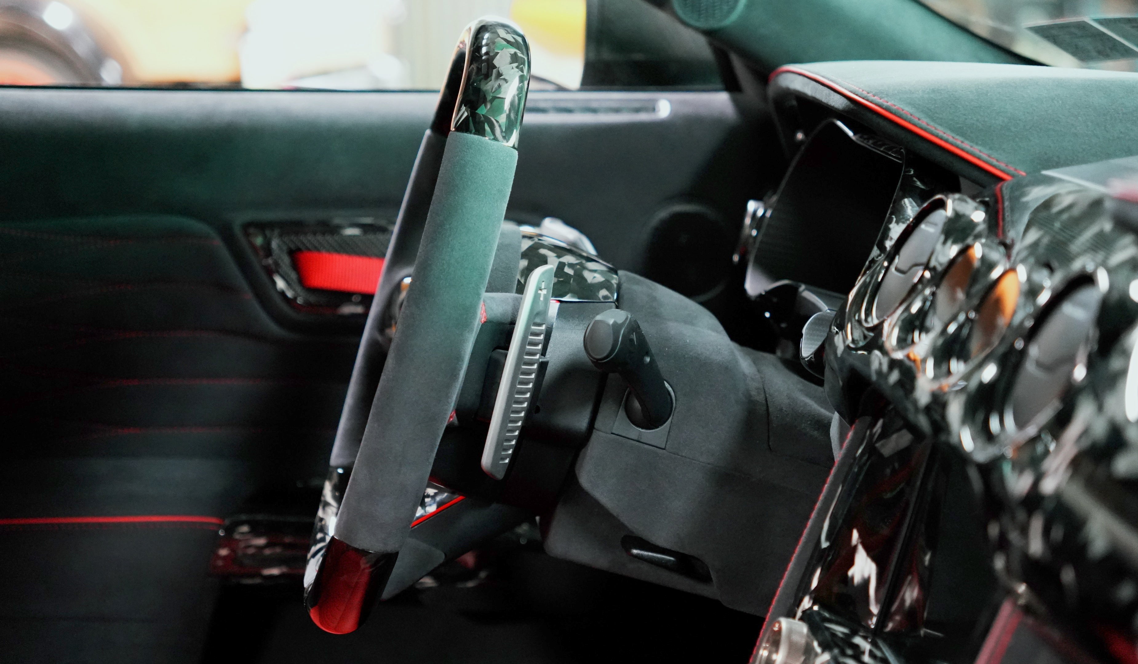 Ford Mustang S550 interior close-up showing UkieCarbon forged carbon fiber steering wheel with Alcantara grips, paddle shifters, and forged carbon dash trim with red stitching.