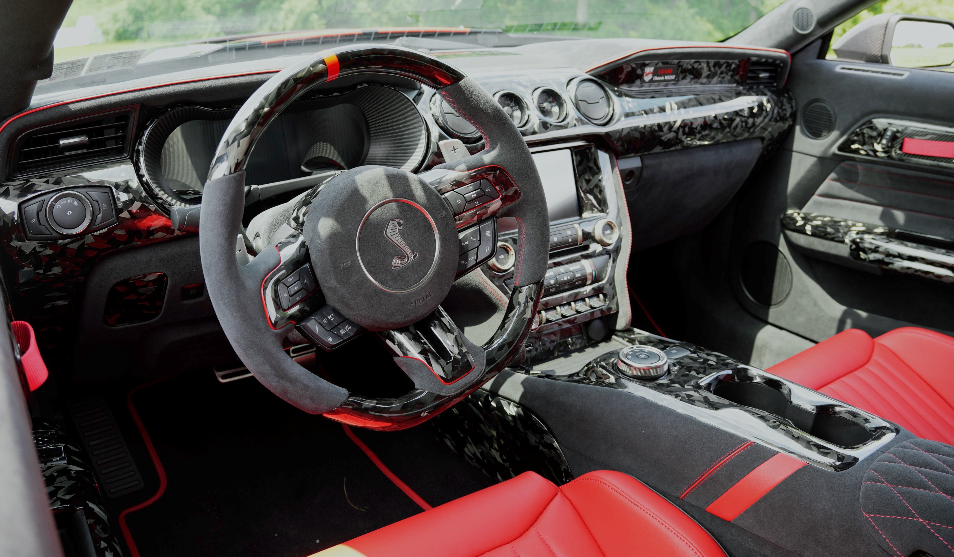 Ford Mustang S550 custom interior by UkieCarbon with forged carbon fiber steering wheel, dash trim, center console, and red accents.