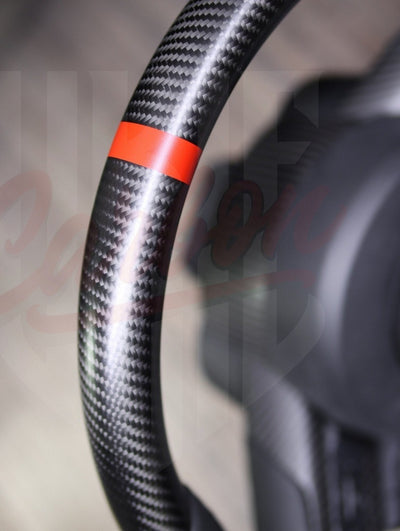 Close-up of gloss carbon fiber finish on a custom Mustang steering wheel with red center stripe.